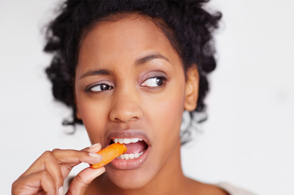 Woman unhappily eating raw carrot