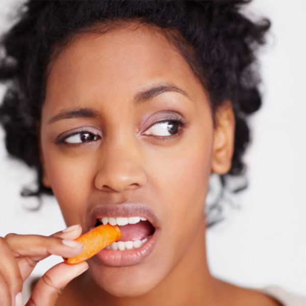 Woman unhappily eating raw carrot